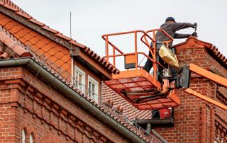 un couvreur sur une nacelle répare un toit en tuiles